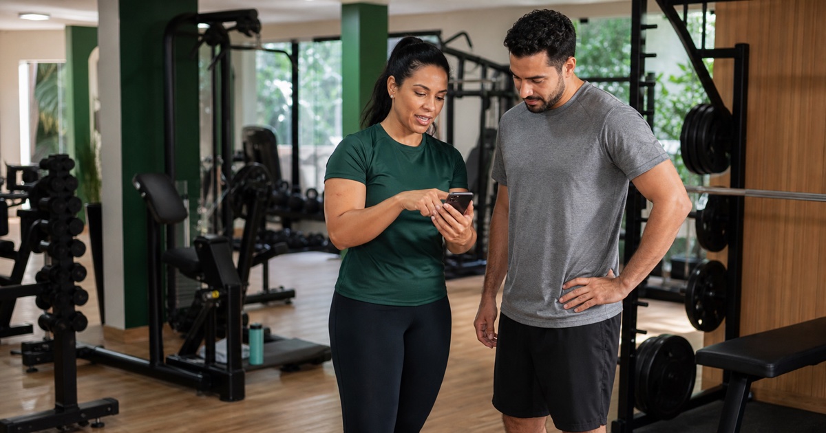 Personal trainer e aluno consultando um plano de treino no celular em uma academia